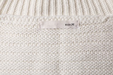 Photo of Clothing label on beautiful beige garment, top view