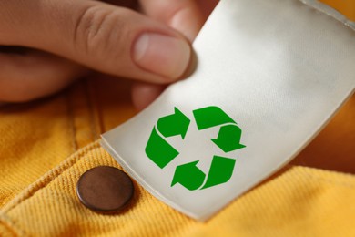 Woman showing clothing label with recycling symbol on yellow jeans, closeup