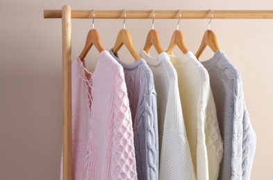 Photo of Collection of warm sweaters hanging on rack near light wall