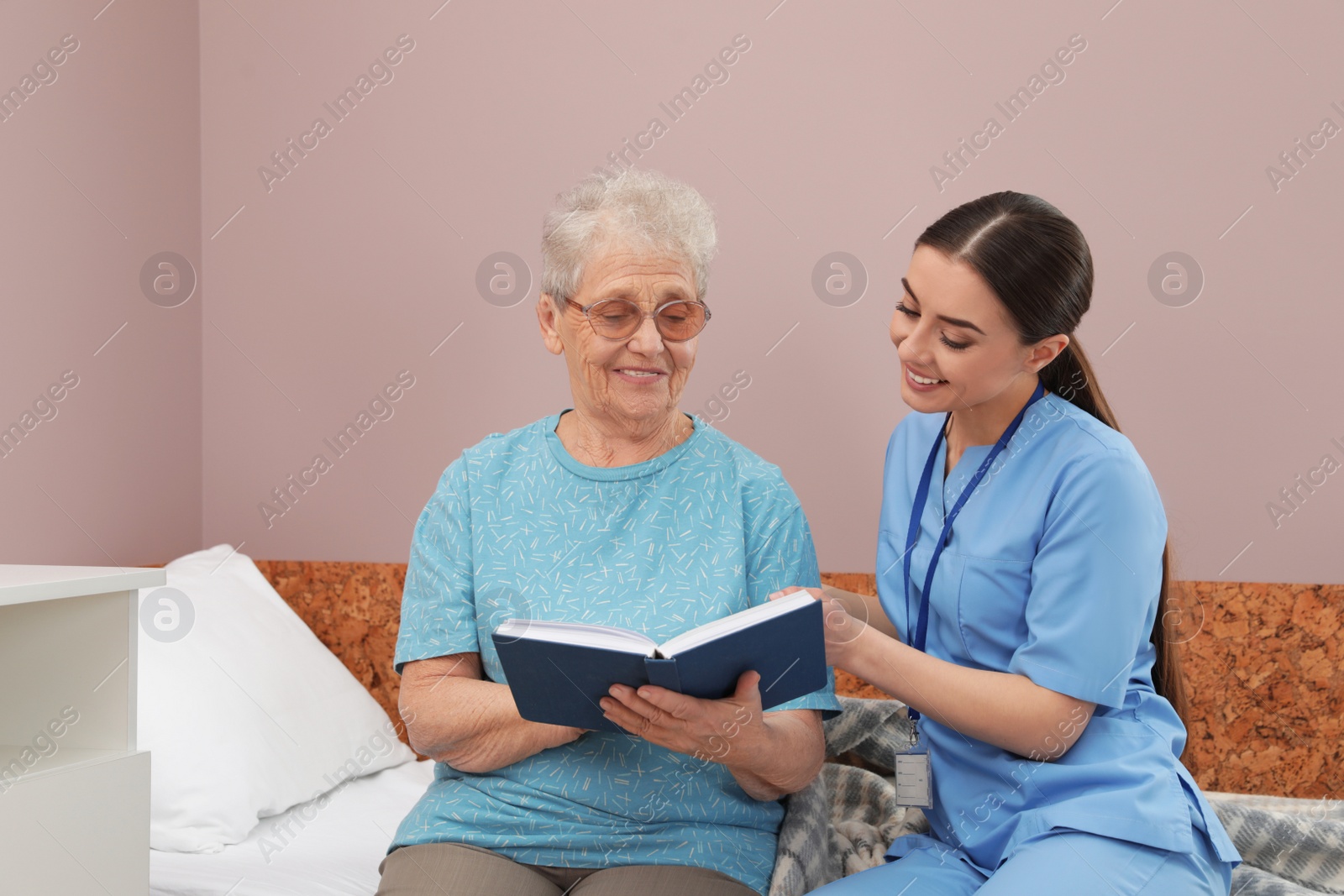 Photo of Nurse reading book with senior woman in hospital ward. Medical assisting