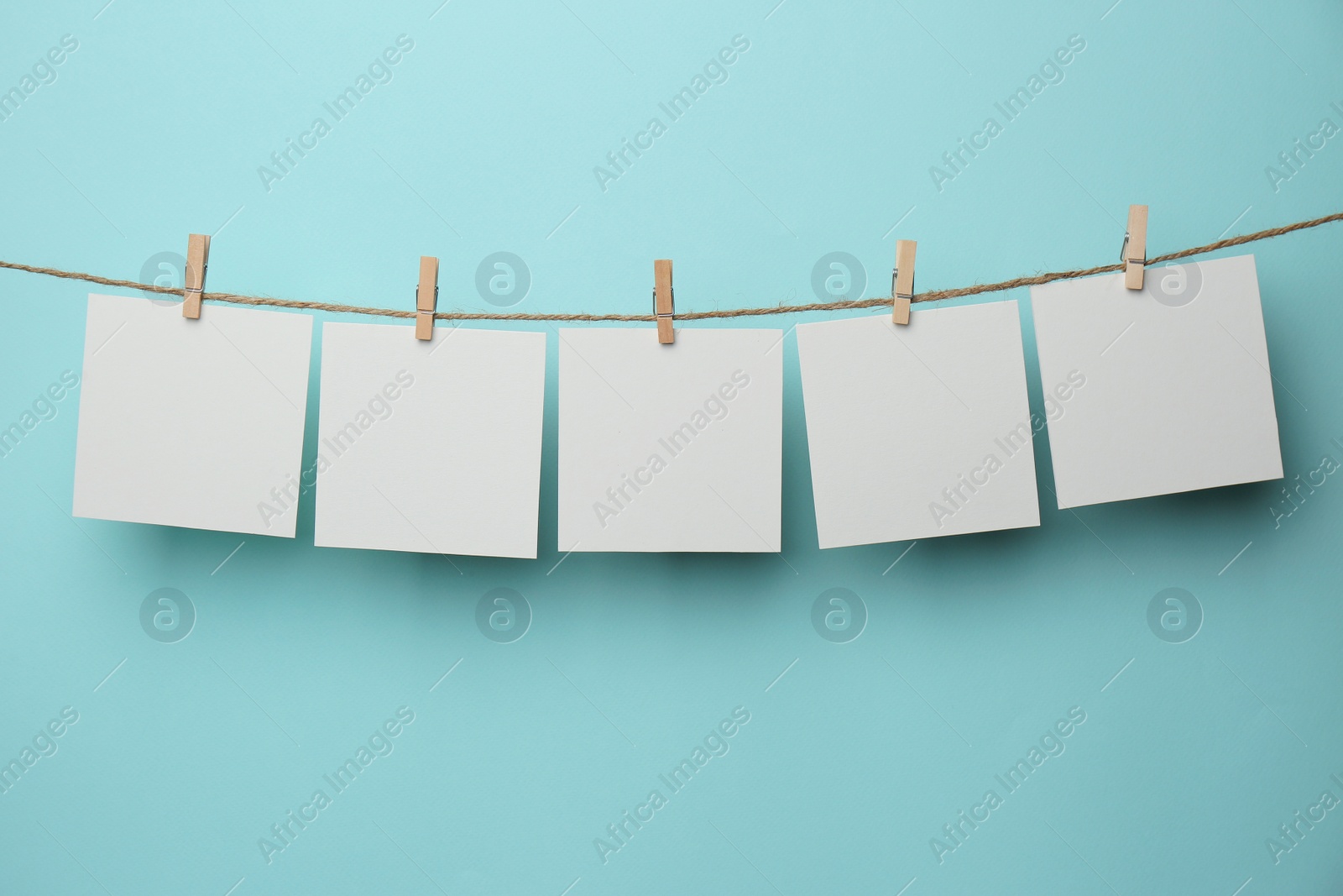 Photo of Wooden clothespins with blank notepapers on twine against light blue background. Space for text