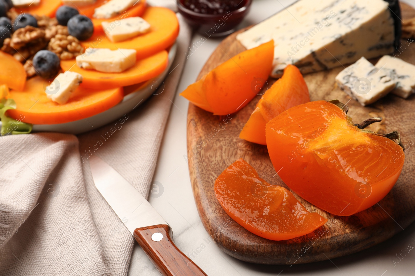 Photo of Tasty sliced persimmon and blue cheese on wooden board, closeup