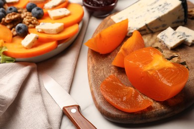 Tasty sliced persimmon and blue cheese on wooden board, closeup