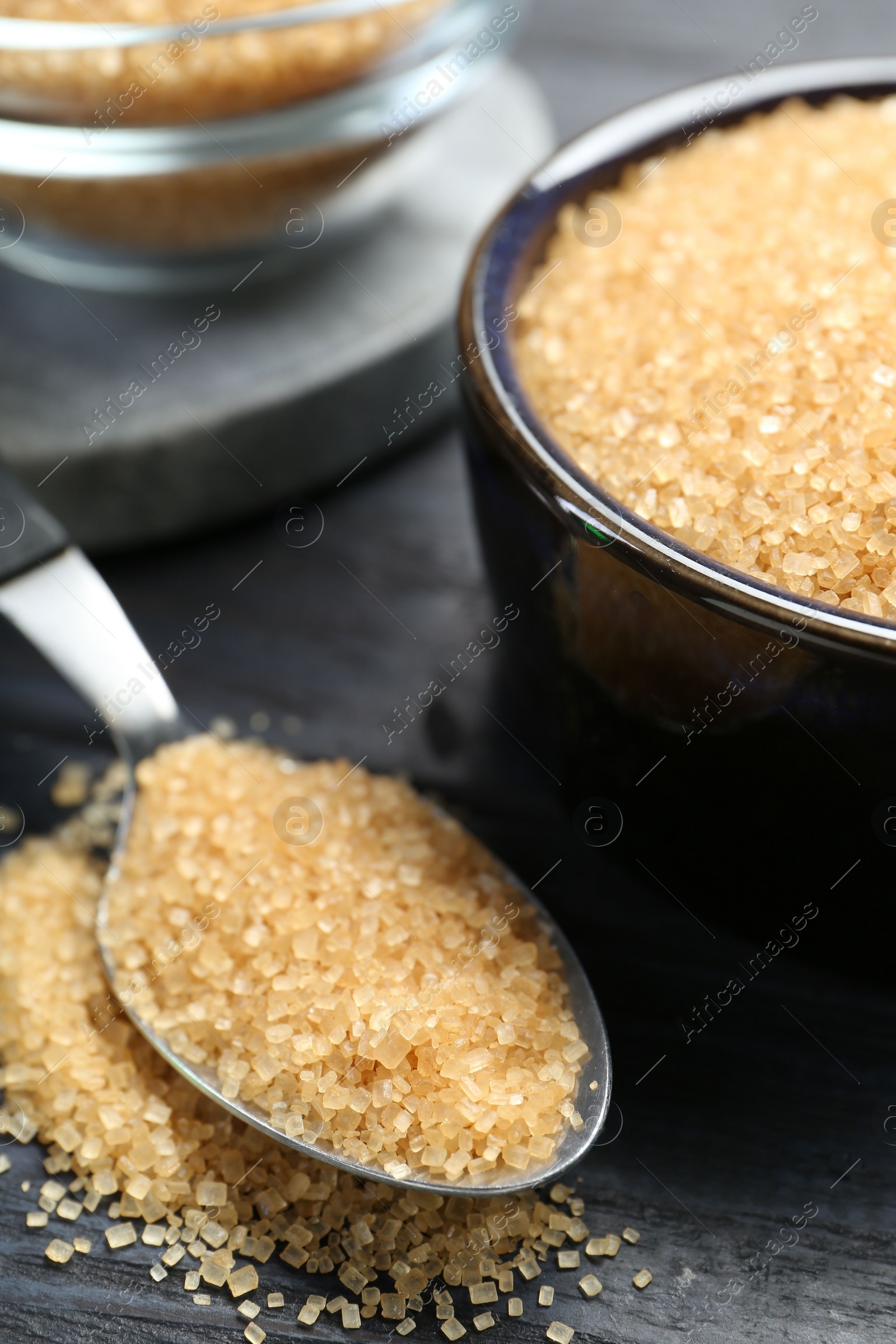 Photo of Brown sugar in bowl and spoon on black wooden table, closeup