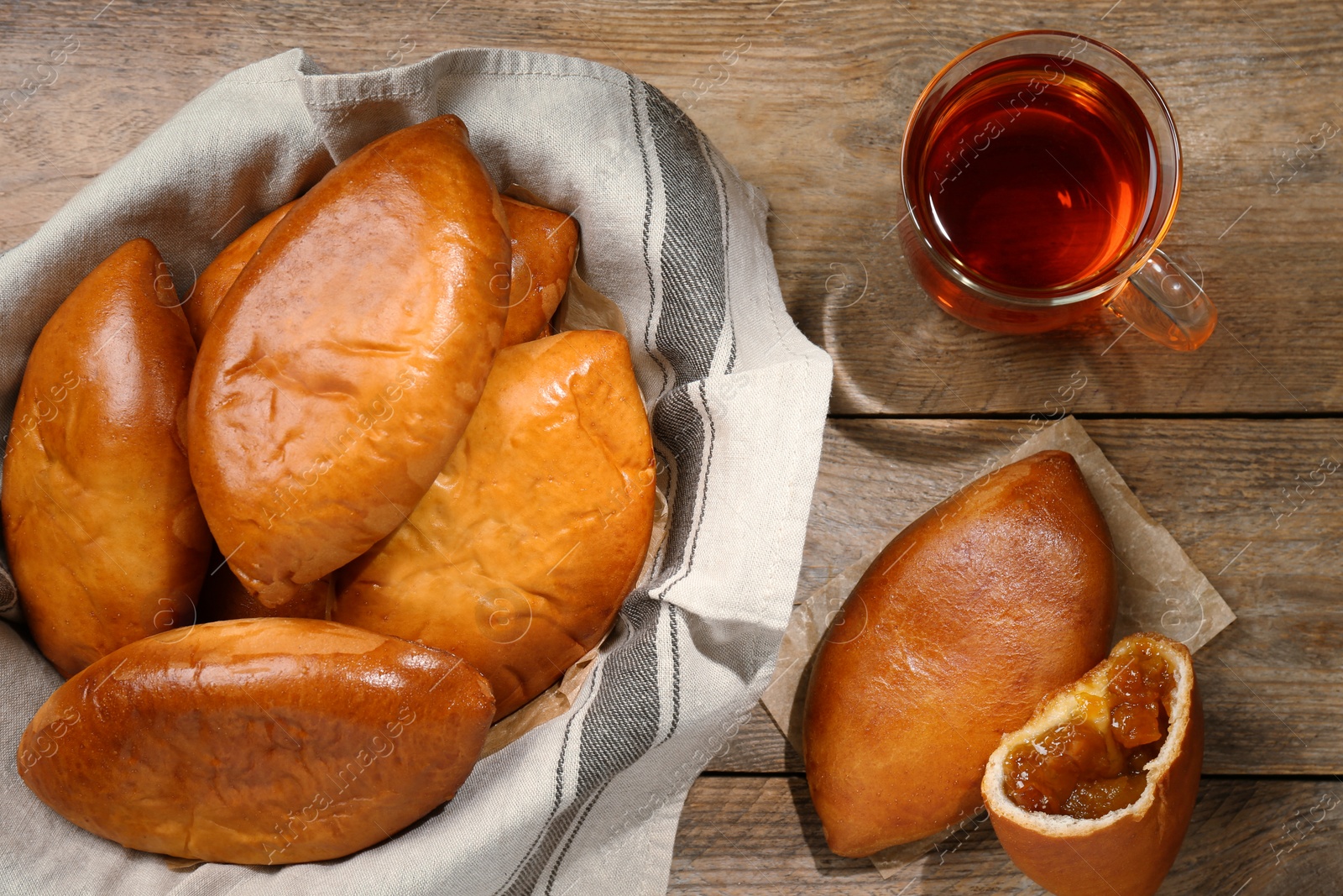 Photo of Many delicious baked patties and glass cup of tea on wooden table, flat lay