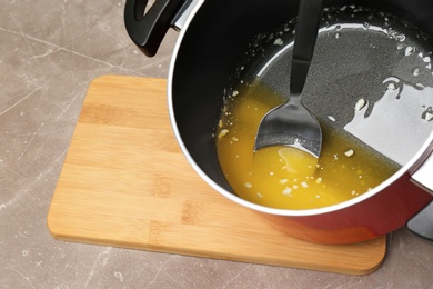 Pot with melting butter and spoon on grey table, closeup. Space for text