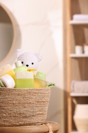 Wicker basket with baby cosmetic products, bath accessories and toy bear on wooden table indoors