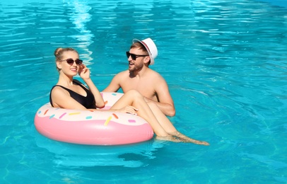 Happy young couple with inflatable ring in swimming pool