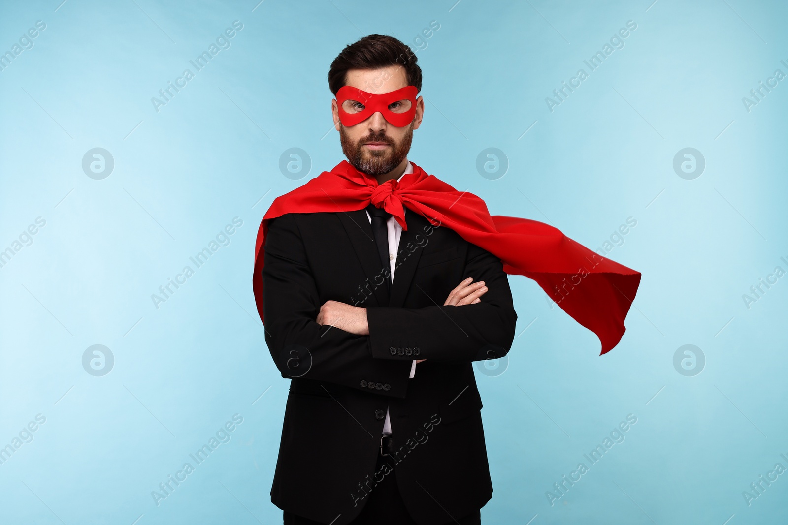 Photo of Businessman wearing red superhero cape and mask on light blue background