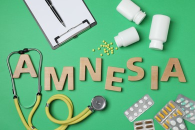 Photo of Word Amnesia made of wooden letters, stethoscope, clipboard and pills on green background, flat lay