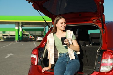 Beautiful young woman with coffee near car at gas station