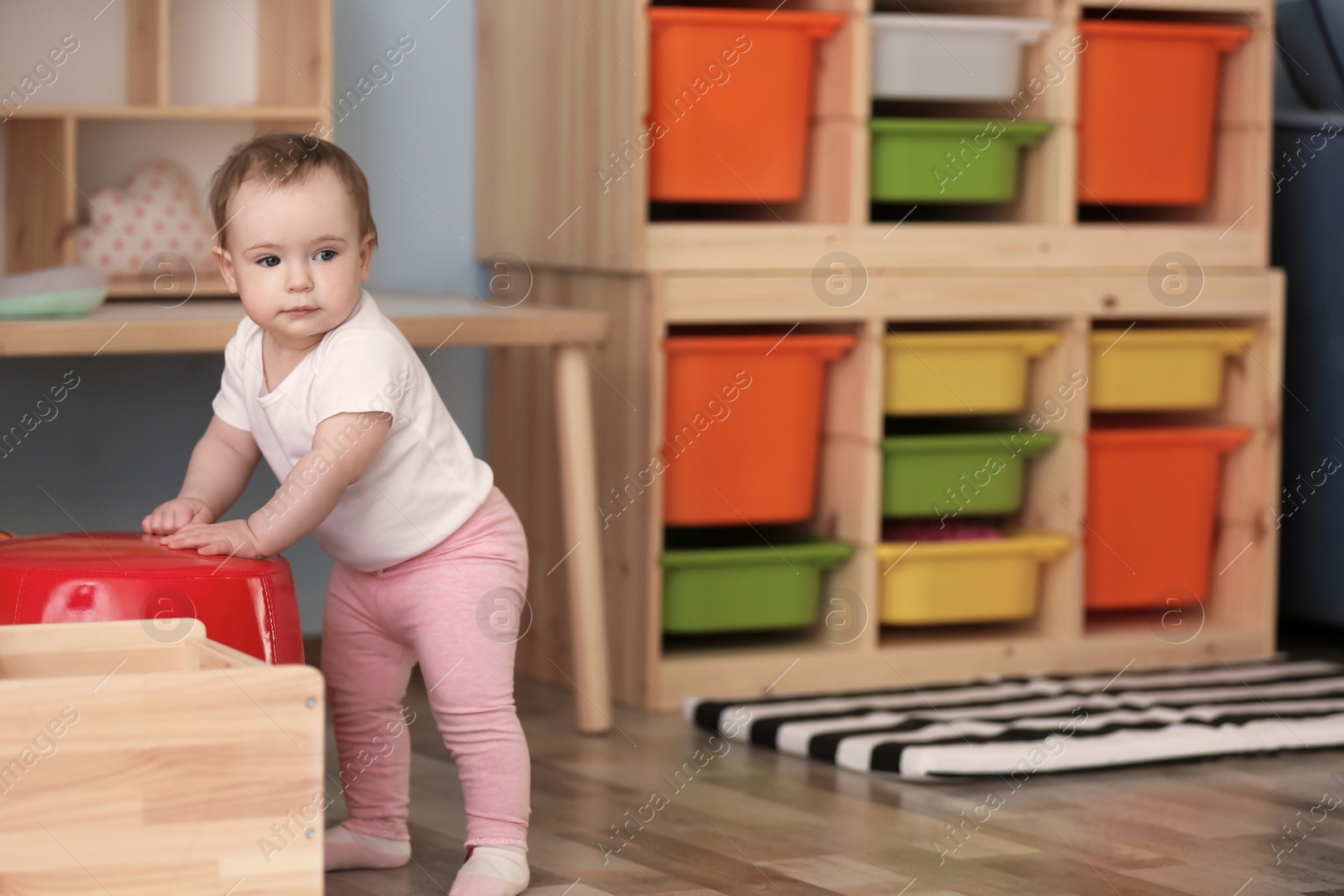 Photo of Cute baby holding on to pouf at home. Learning to walk