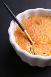 Photo of Delicious creme brulee in bowl and spoon on dark gray table, closeup