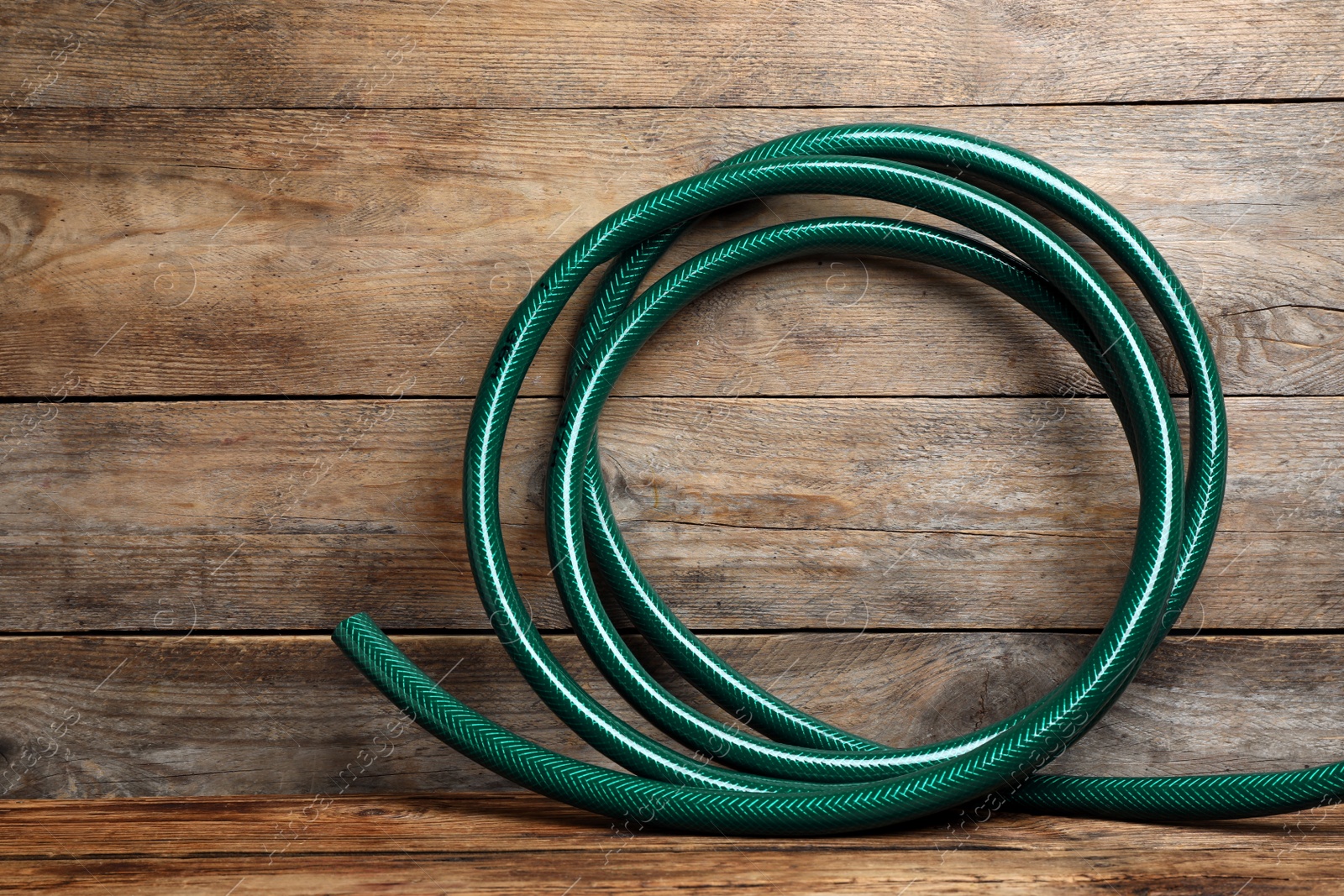 Photo of New green garden hose on wooden table