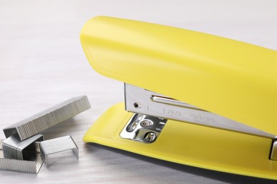 Yellow stapler with staples on light wooden table, closeup