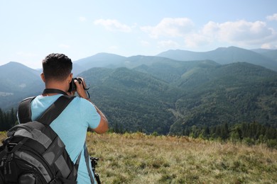 Photo of Professional photographer taking picture with modern camera in mountains, back view. Space for text