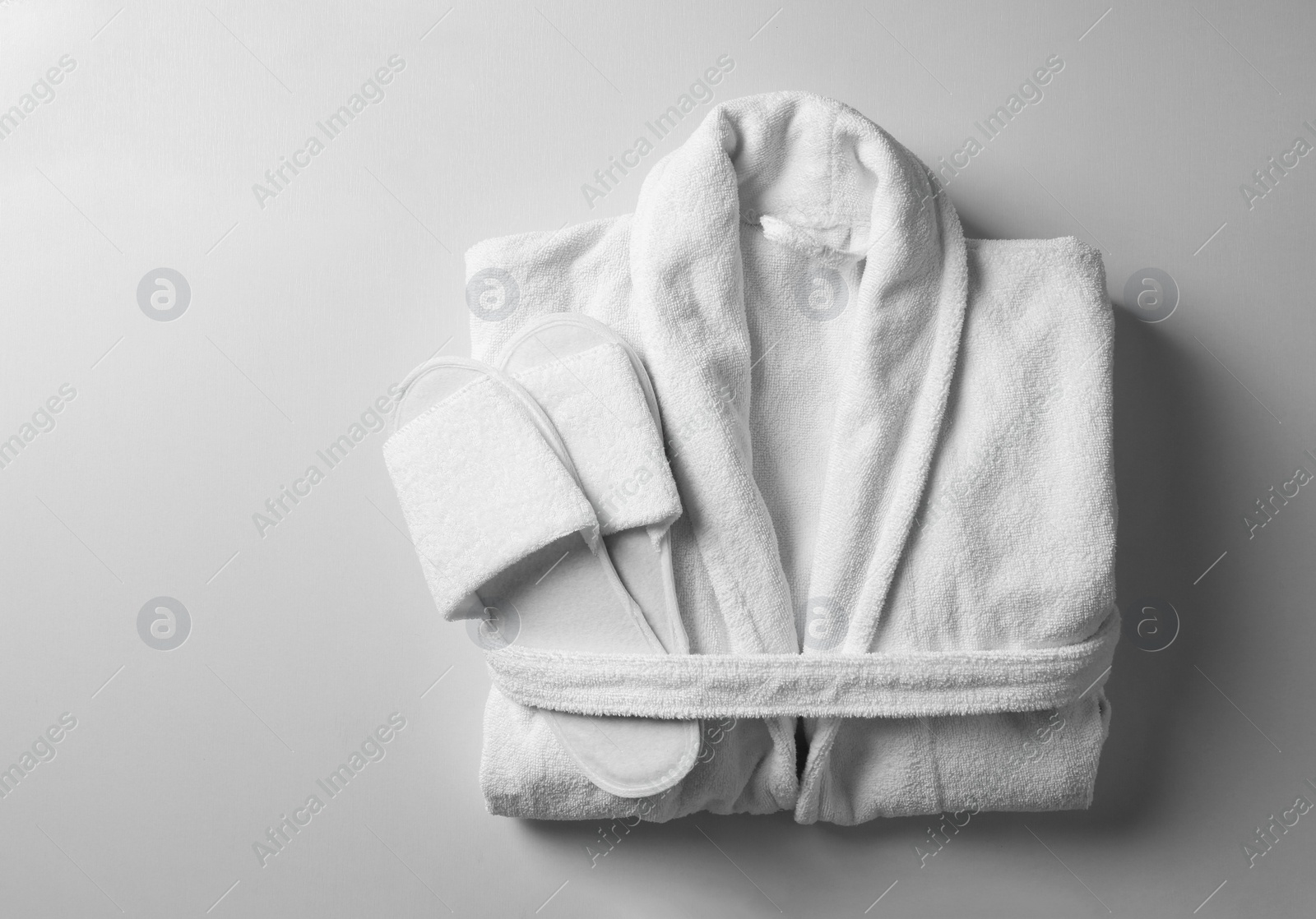 Photo of Clean folded bathrobe and slippers on white background, top view