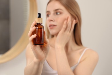 Photo of Woman with bottle of essential oil indoors, selective focus. Space for text