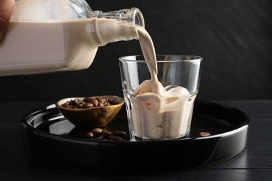 Photo of Pouring coffee cream liqueur into glass at black wooden table, closeup