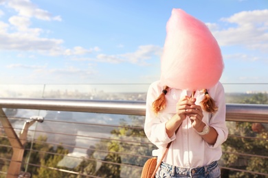 Photo of Young woman with cotton candy outdoors on sunny day. Space for text