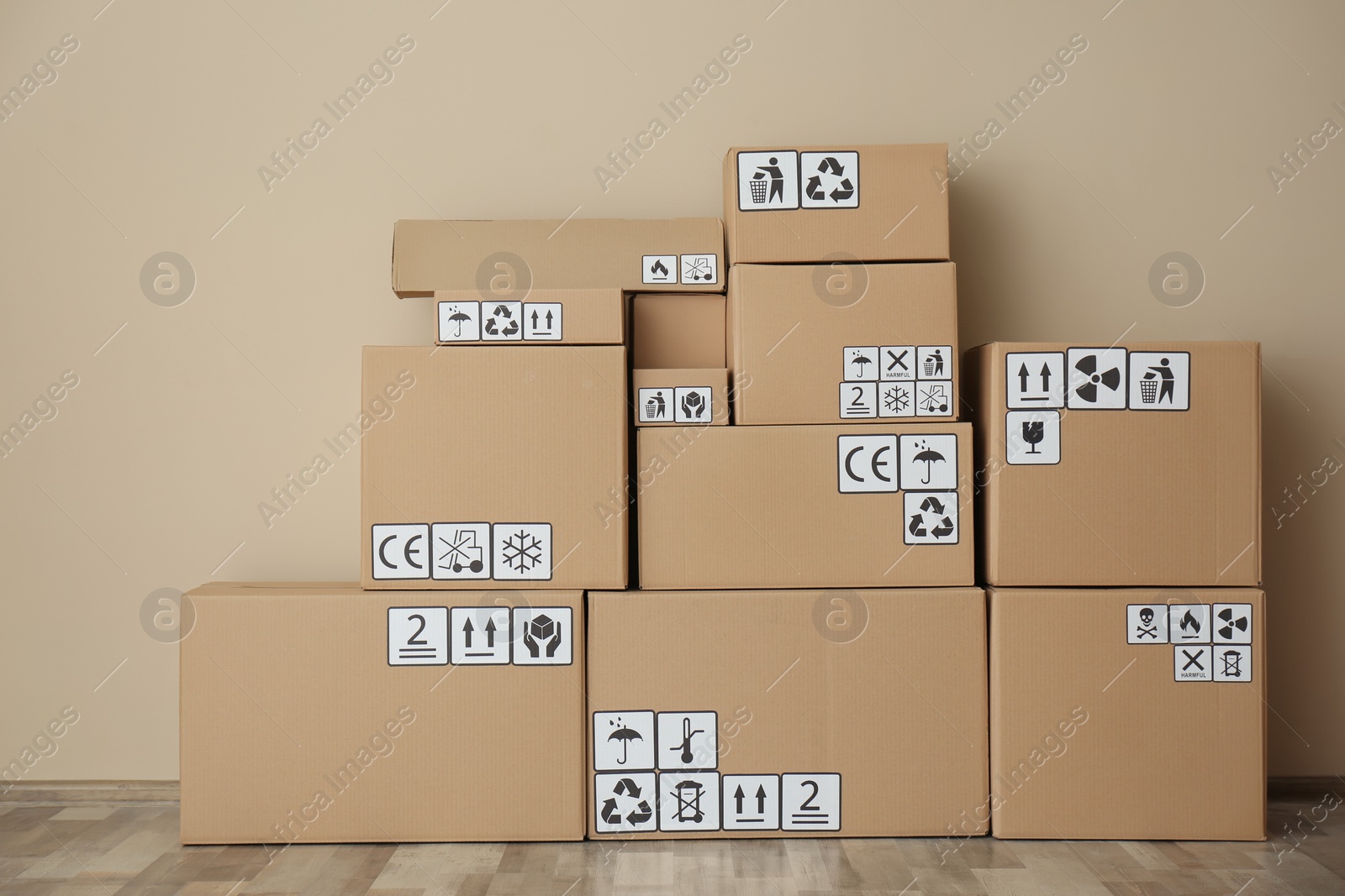 Photo of Cardboard boxes with different packaging symbols on floor near beige wall. Parcel delivery