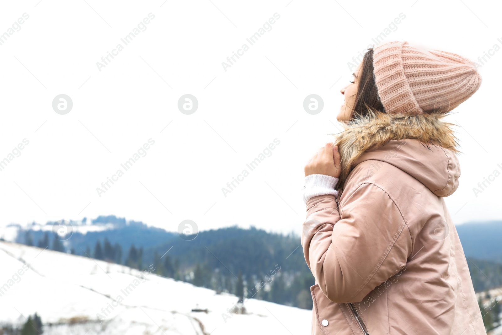 Photo of Young woman in warm clothes near snowy hill, space for text. Winter vacation