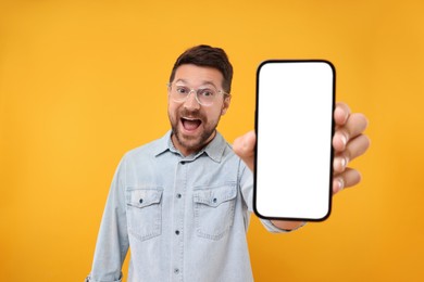 Surprised man showing smartphone in hand on yellow background