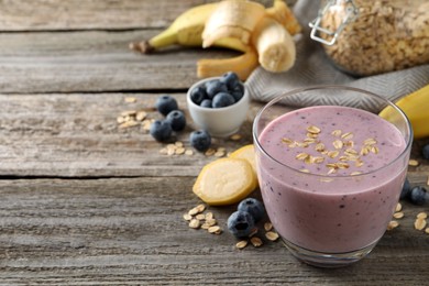 Photo of Glass of tasty banana blueberry smoothie with oatmeal on wooden table, space for text