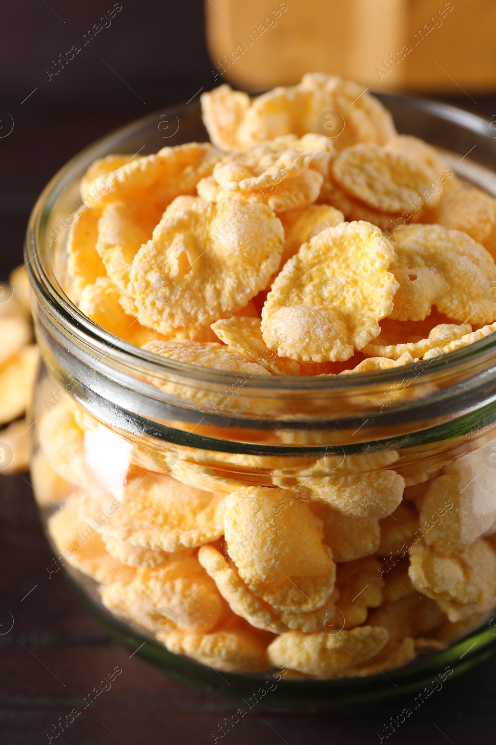 Photo of Jar of tasty crispy corn flakes on wooden table, closeup