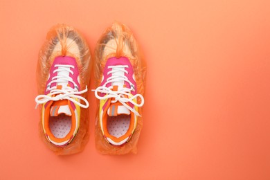 Photo of Women's sneakers in shoe covers on coral background, top view. Space for text