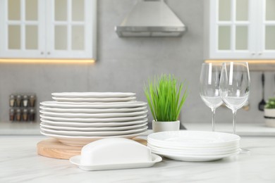 Photo of Clean plates, glasses, butter dish and floral decor on white marble table in kitchen