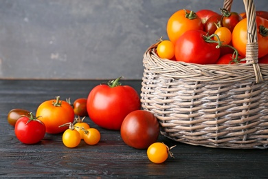 Composition with fresh ripe tomatoes and wicker basket on wooden table