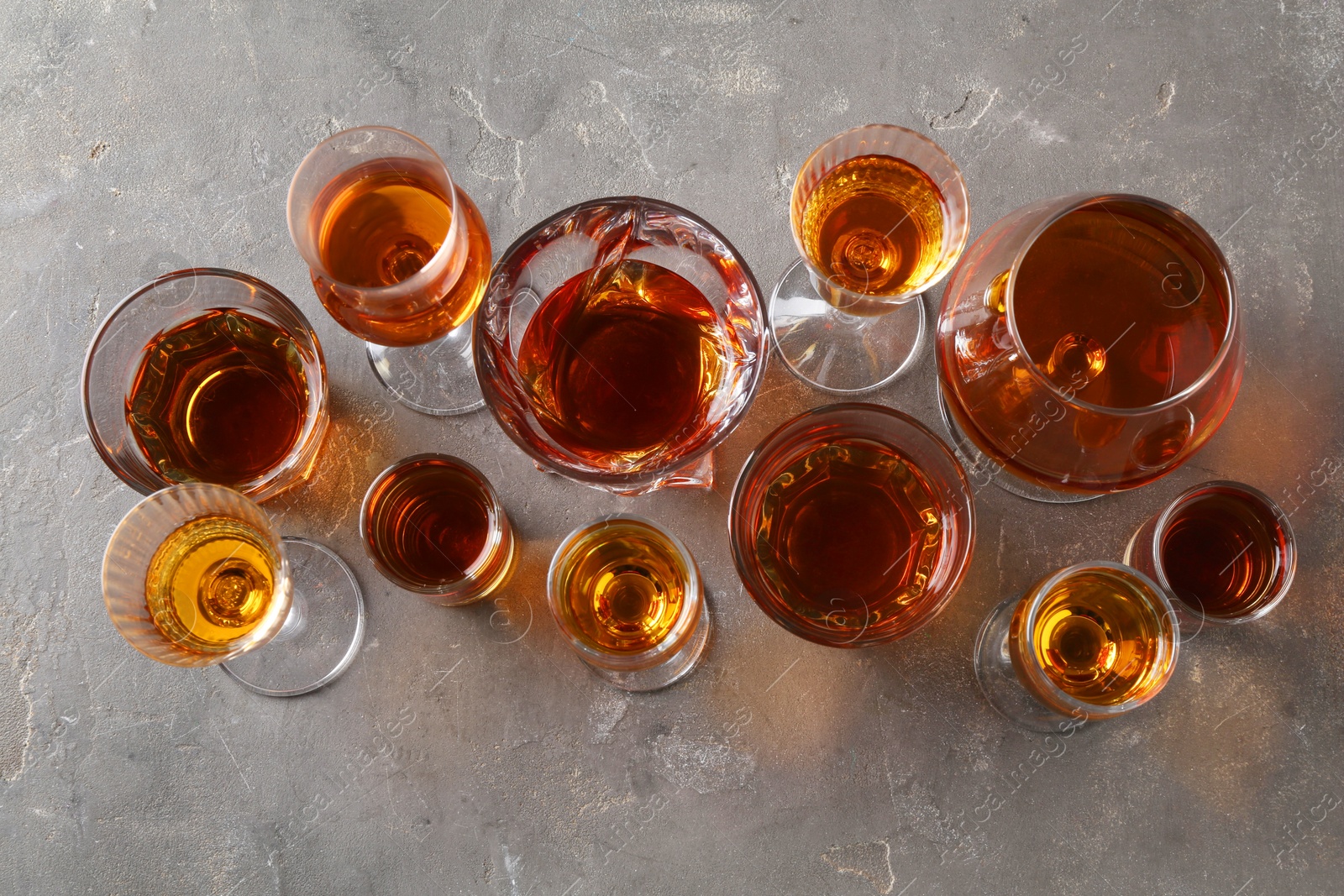 Photo of Different delicious liqueurs in glasses on grey table, flat lay