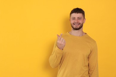 Young man showing heart gesture on orange background, space for text