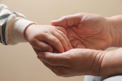 Photo of Woman holding hands with her granddaughter on beige background, closeup