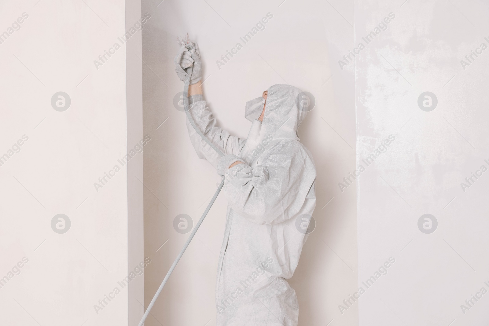 Photo of Decorator in uniform painting wall with sprayer indoors