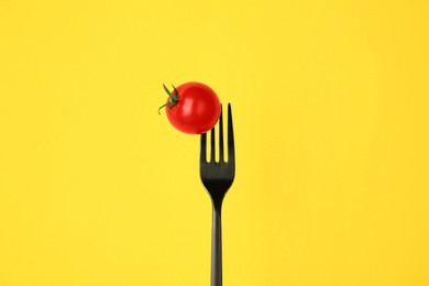 Photo of Fork with cherry tomato on yellow background