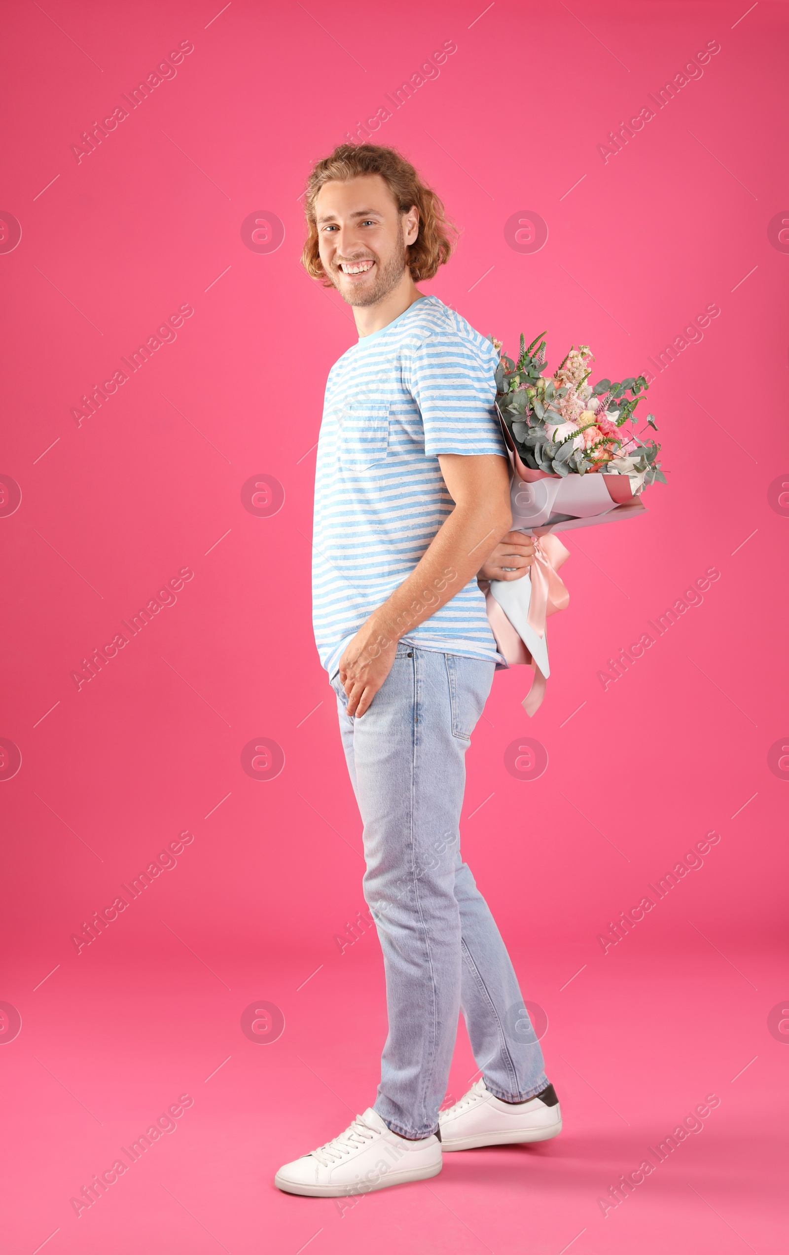 Photo of Young handsome man hiding beautiful flower bouquet behind his back on pink background