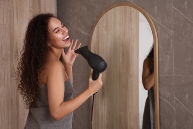 Photo of Beautiful African American woman singing while using hair dryer near mirror in bathroom, space for text