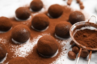 Photo of Delicious chocolate truffles with cocoa powder and hazelnuts on white table, closeup