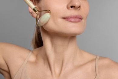Photo of Woman massaging her face with jade roller on grey background, closeup