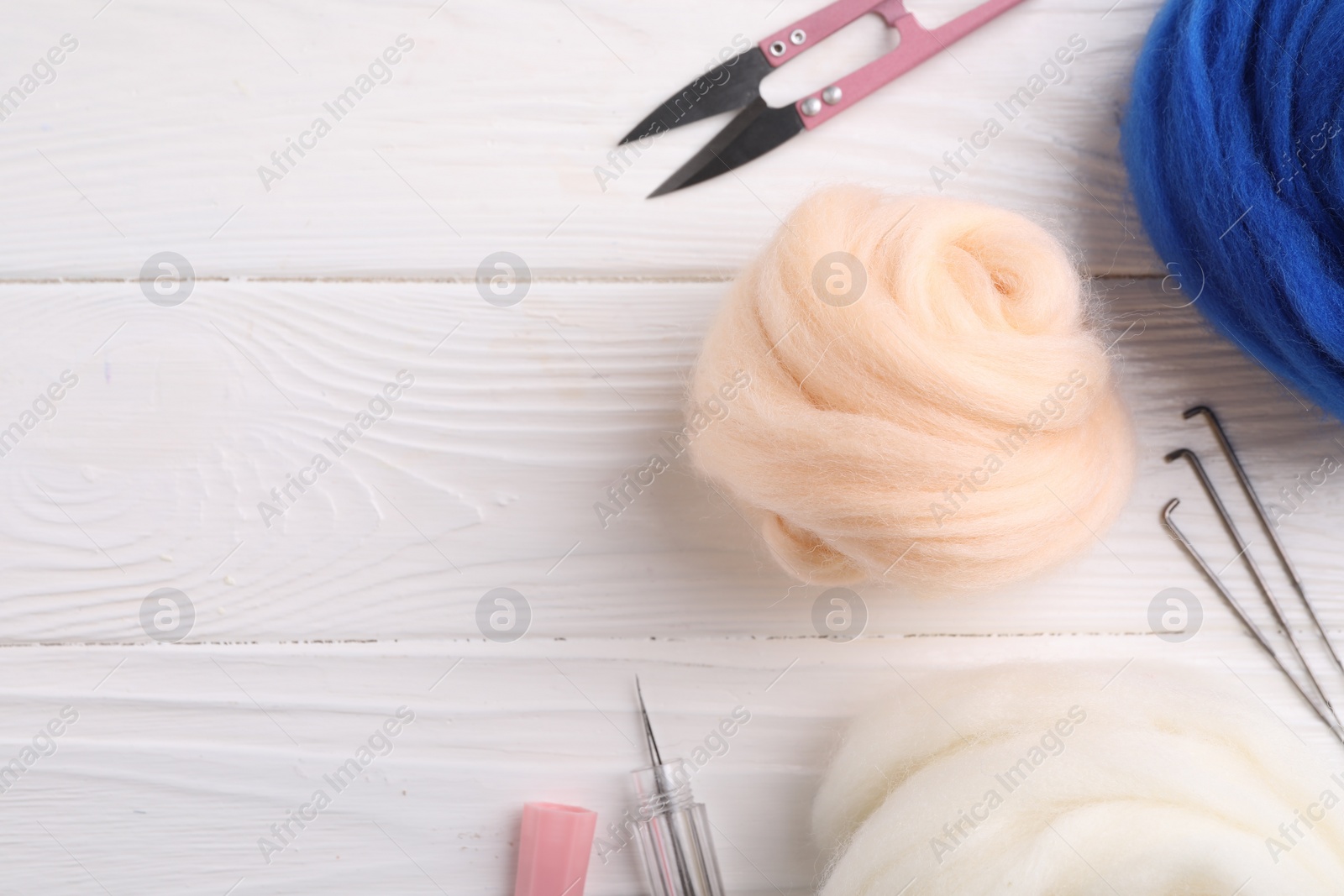 Photo of Felting wool, scissors and needles on white wooden table, flat lay. Space for text