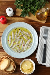 Photo of Tasty pickled anchovies with spices and products on wooden table, flat lay