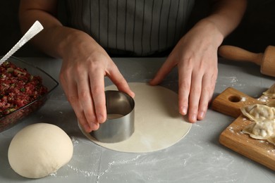 Photo of Woman cutting dough for gyoza at grey table, closeup
