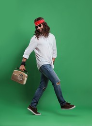 Photo of Stylish hippie man in sunglasses with retro radio receiver walking on green background