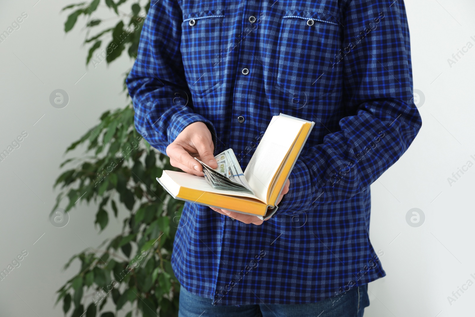 Photo of Man hiding dollar banknotes in book indoors, closeup. Money savings