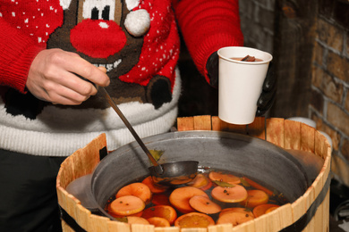 Photo of Seller filling cup with tasty mulled wine at winter fair, closeup