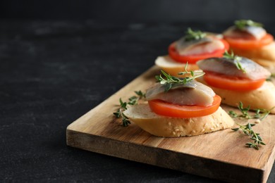 Delicious sandwiches with salted herring, tomato and thyme on black table, closeup. Space for text