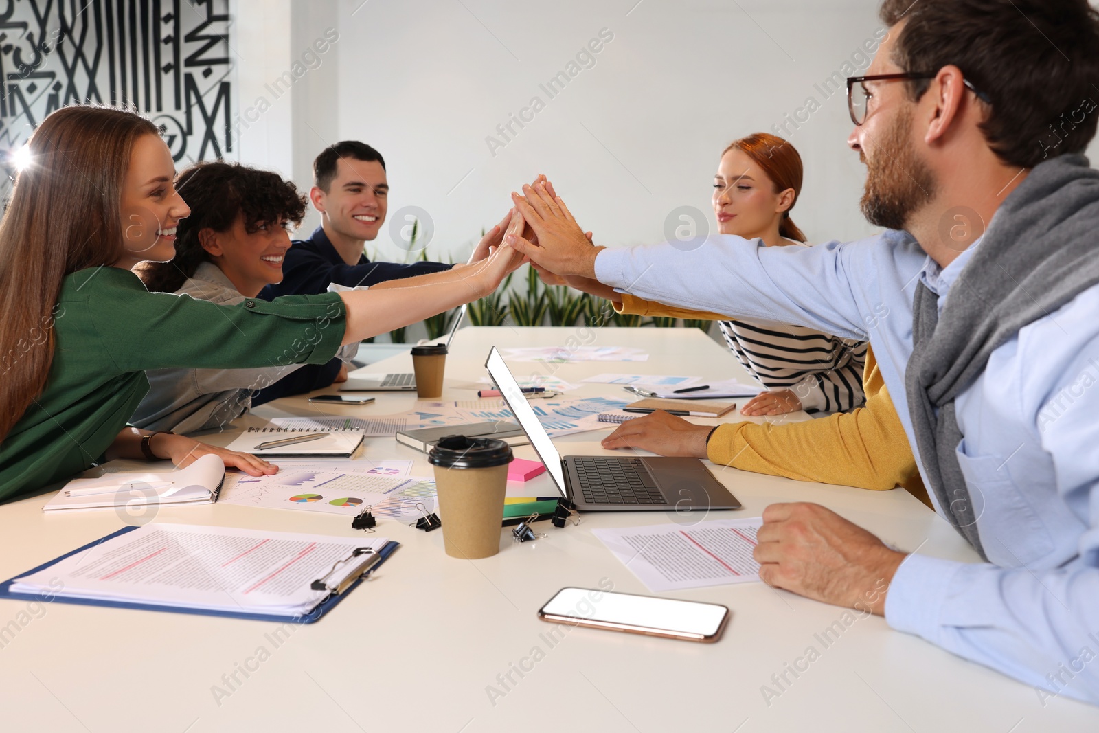 Photo of Team of employees joining hands at white table in office. Startup project