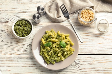 Photo of Flat lay composition with plate of delicious basil pesto pasta on wooden table